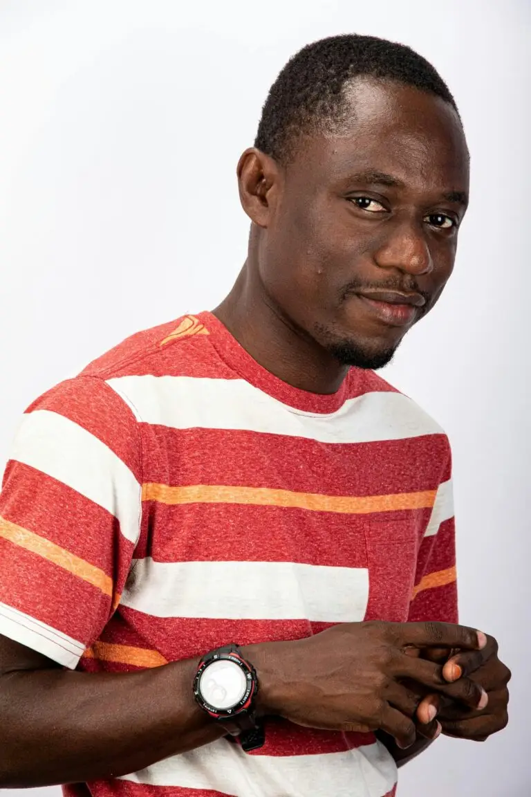 Casual portrait of a smiling man in a red striped t-shirt with a watch, set against a white background.